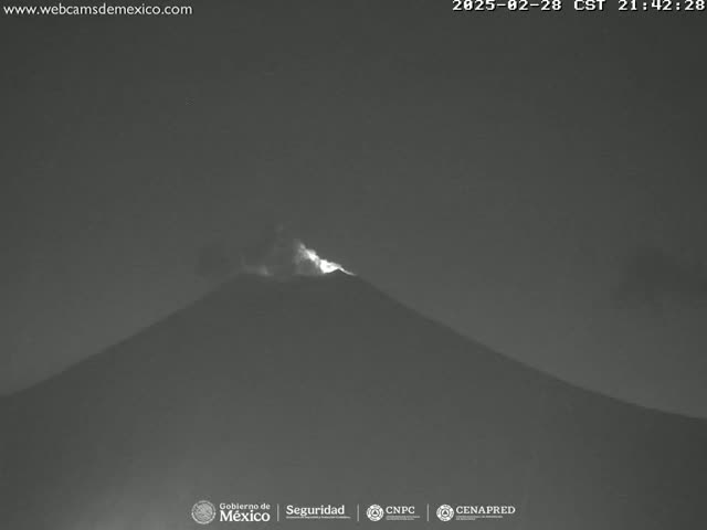 A nighttime, low-light image shows a volcano emitting a faint glow from its summit under a dark sky.