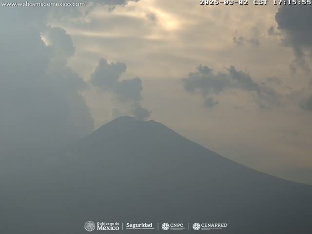 A hazy, partly cloudy sky hangs over a large, dark-colored mountain.