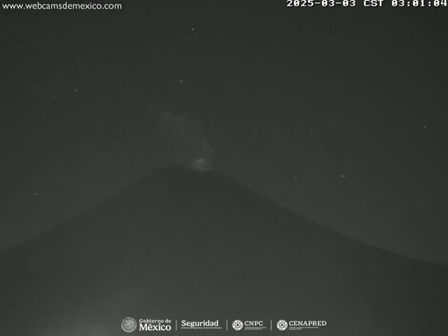 A dark, nighttime view shows a volcano emitting a faint glow under a clear, starry sky.