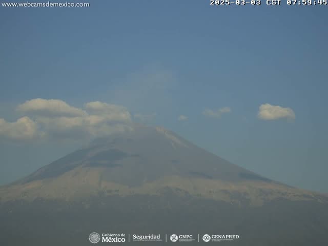 A large, hazy mountain is visible under a mostly clear sky with a few small cumulus clouds.