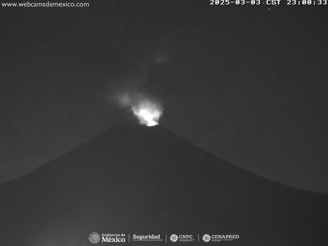 A volcano erupts at night, emitting a glowing plume of smoke and ash into the dark sky.
