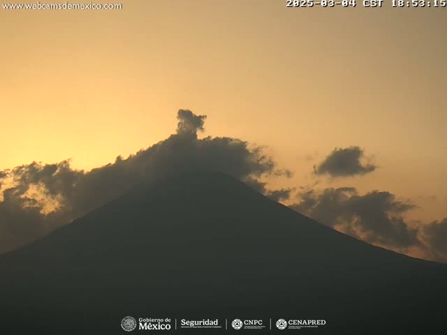 A large, dark mountain is silhouetted against a pale orange sunset sky with some clouds.