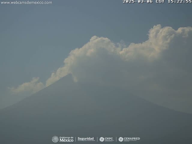 A hazy mountain is partially obscured by a layer of clouds under a mostly clear sky.