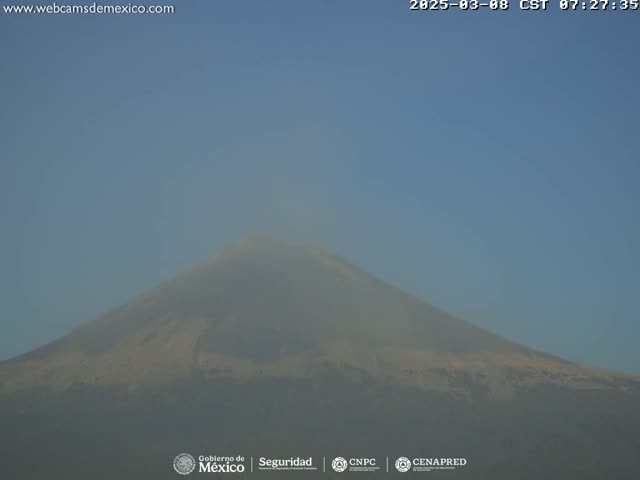 A hazy, light-brown mountain is visible under a clear, light-blue sky.