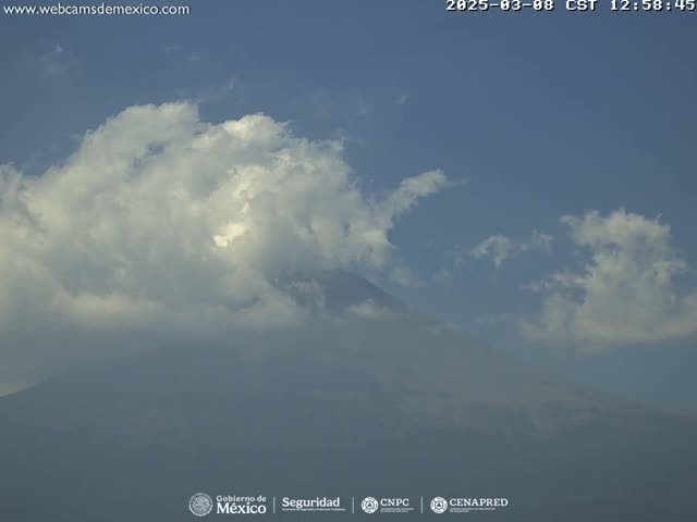 A large, fluffy cloud partially obscures a hazy mountain under a mostly clear sky.