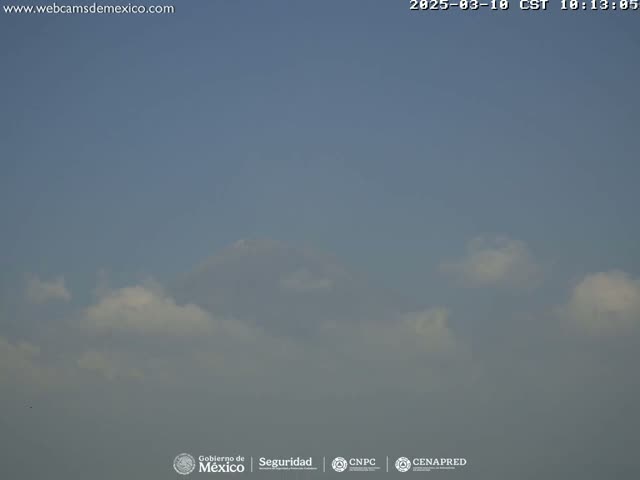 A mostly clear sky with scattered cumulus clouds under hazy conditions is visible.