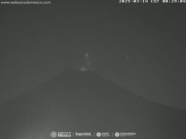 A nighttime, low-light image shows a volcano with a faint glow emanating from its peak under a clear, starry sky.