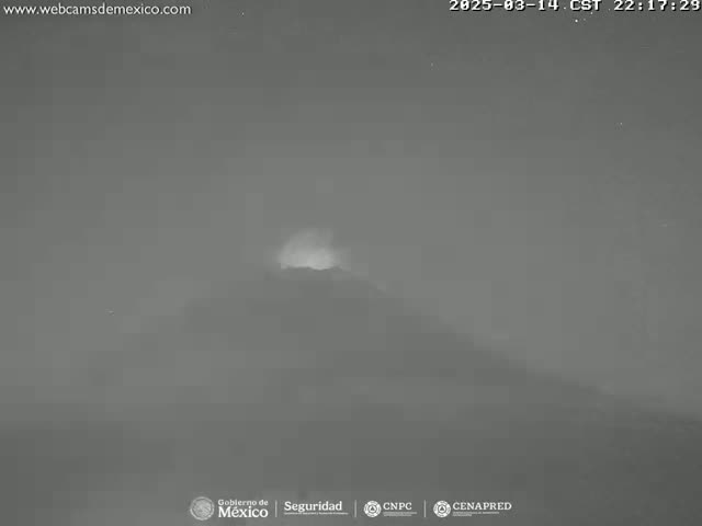 A nighttime, low-light image shows a hazy or foggy mountaintop with a faint glow emanating from its peak.