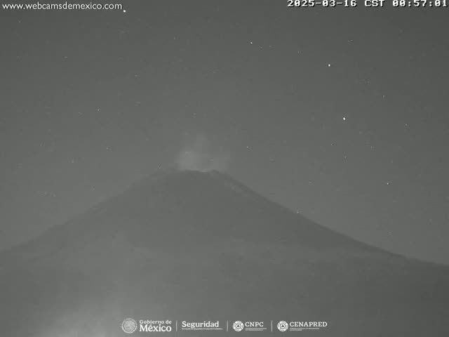 A nighttime, low-light image shows a volcano emitting a faint plume of smoke under a clear, starry sky.