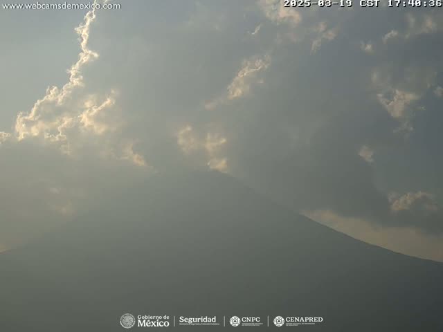 A hazy mountain is partially visible beneath a partly cloudy sky, with sunlight breaking through the clouds.