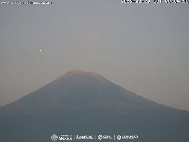 A large, dark-colored mountain is visible under a hazy, light-grey sky.