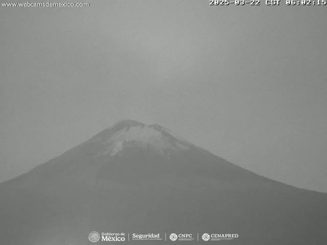 A grayscale long shot shows a snow-capped mountain under a hazy sky.