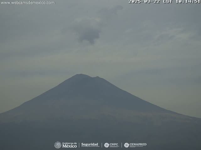 A large, dark-colored mountain is visible under a mostly cloudy, hazy sky.