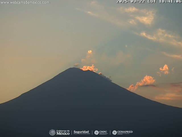 A large, dark mountain is silhouetted against a pale orange and blue sunset sky with a few wispy clouds.