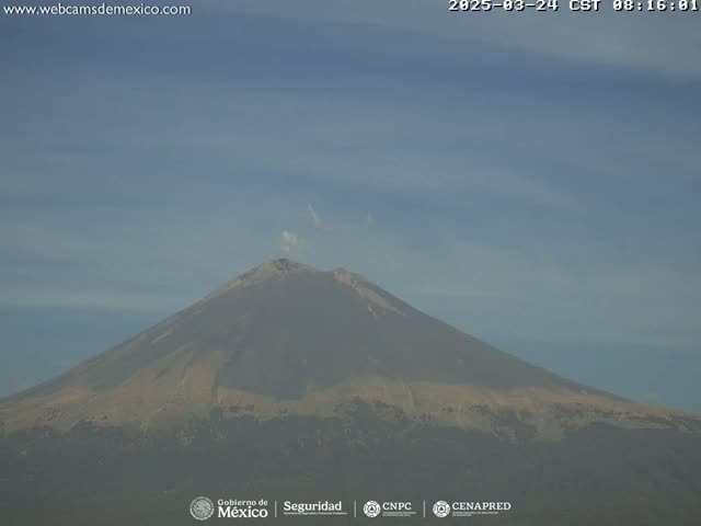 A large, tan-colored volcano with a small plume of smoke emanating from its peak is visible under a hazy sky.