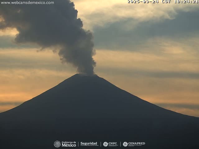 A large, dark volcano emits a plume of dark gray smoke against a pale orange and yellow sunset sky.
