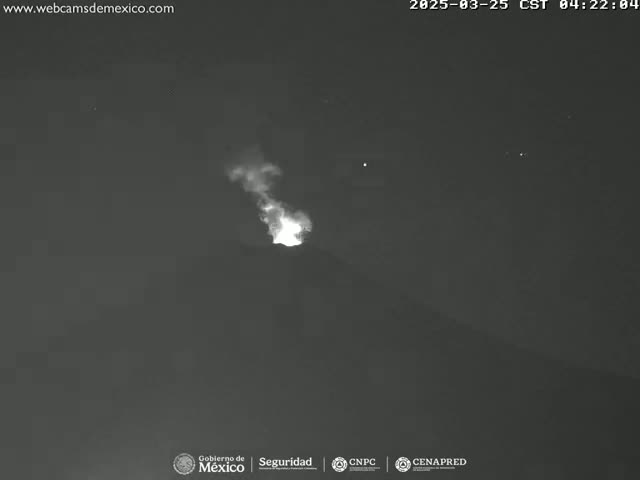 A nighttime, long shot shows a volcano emitting a plume of smoke and what appears to be glowing lava.