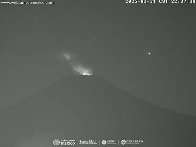 A nighttime, low-light image shows a volcano emitting a faint glow from its summit under a clear, starry sky.