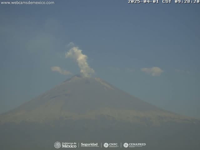 A large volcano with a plume of smoke rising from its summit is visible under a clear sky.