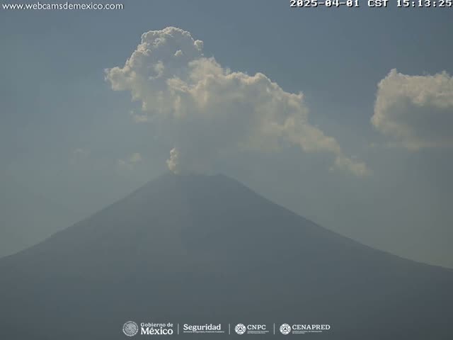 A large volcano is partially obscured by haze under a partly cloudy sky.