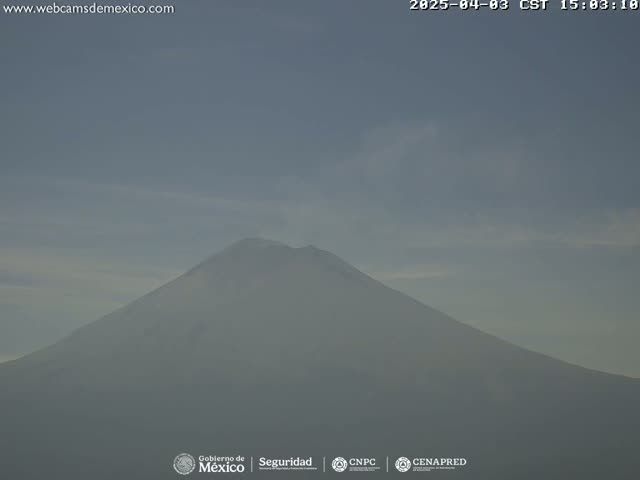 A hazy, overcast sky hangs over a large, volcanic mountain emitting a plume of smoke.
