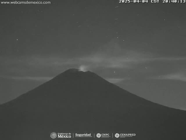 A nighttime, low-light image shows a volcano erupting under a slightly cloudy sky speckled with stars.