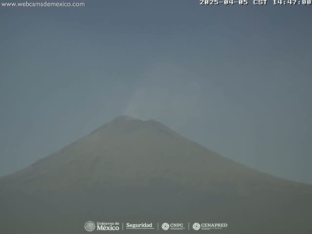 A hazy, light-grey volcano emits a thin plume of smoke under a clear sky.