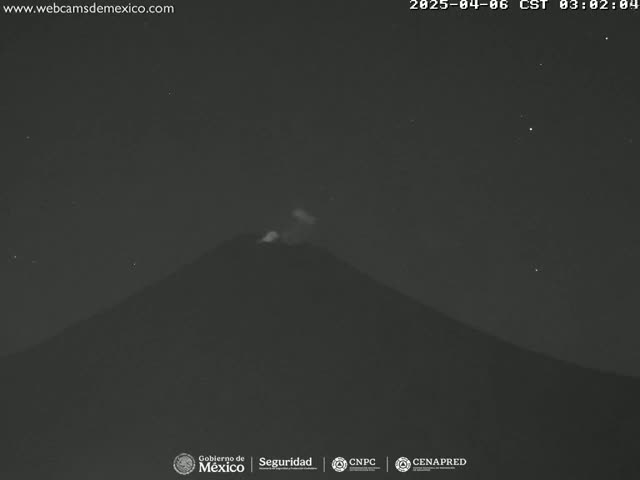 A dark, nighttime image shows a volcano emitting a small amount of smoke or ash under a clear, starry sky.