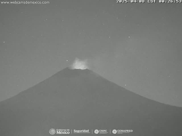 A grayscale nighttime image shows a volcano emitting a faint plume of smoke under a starry sky.