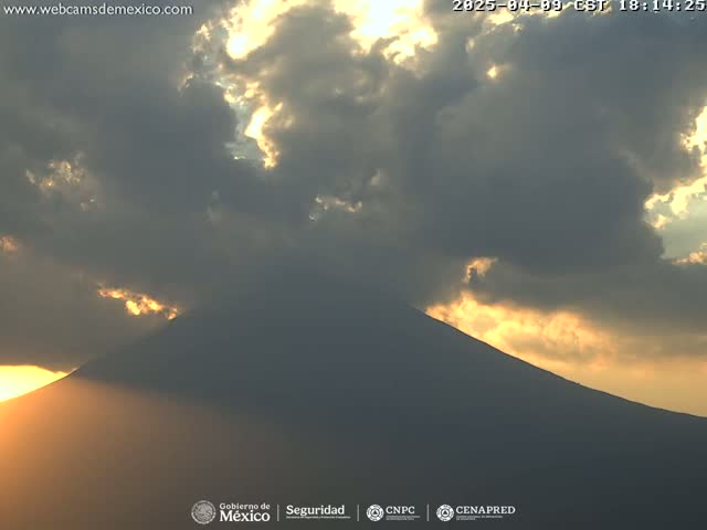 A large, dark mountain silhouetted against a sunset sky filled with mostly dark clouds, with rays of sunlight breaking through.