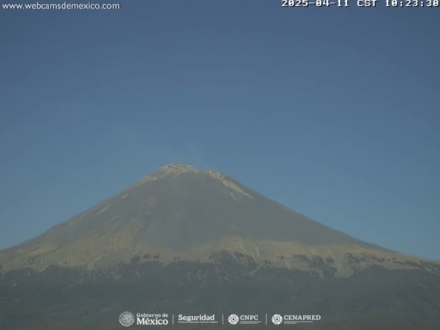 A large, tan-colored volcano is seen on a clear day under a pale blue sky.