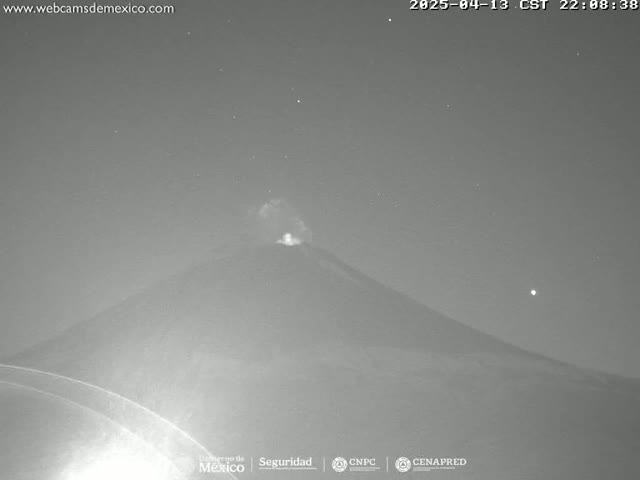 A dark, nighttime view shows a volcano emitting a faint glow under a clear, starry sky.