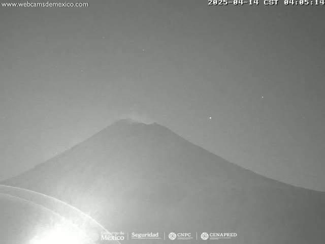 A nighttime, low-light grayscale image shows a large, dark mountain, possibly a volcano, under a clear, starry sky.