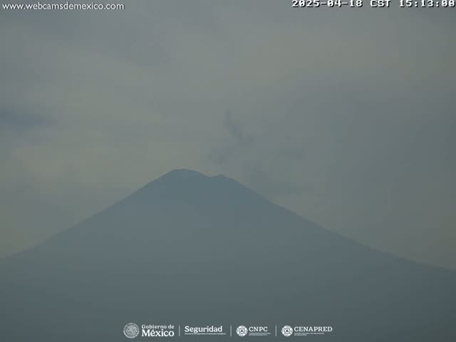 A hazy view shows a large, dark mountain under a mostly cloudy sky.