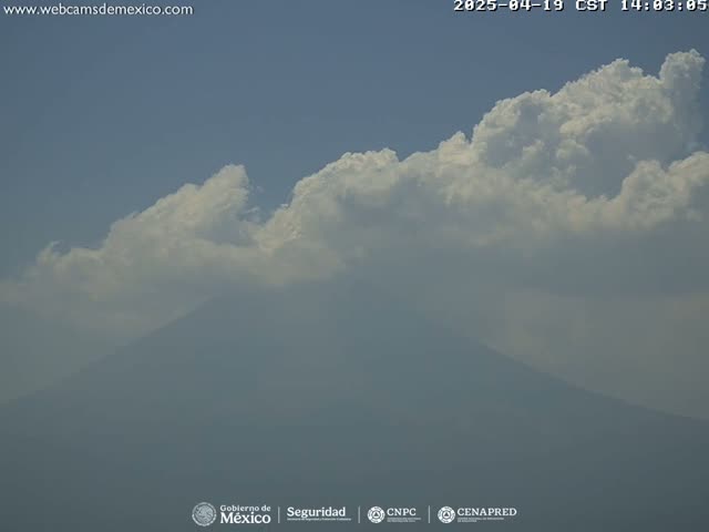 A hazy mountain is partially obscured by a large, bright white cloud formation under a mostly clear sky.