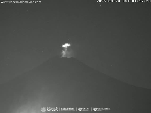 A nighttime, low-light image shows a volcano erupting with a bright plume of ash and smoke.