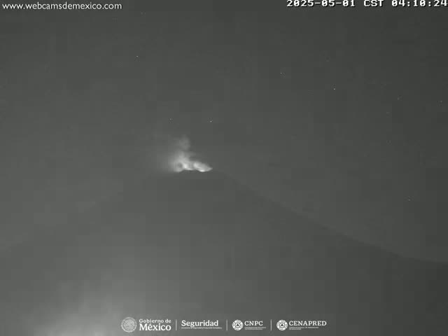 A nighttime, low-light image shows a volcano emitting a plume of smoke and ash under a clear, starry sky.