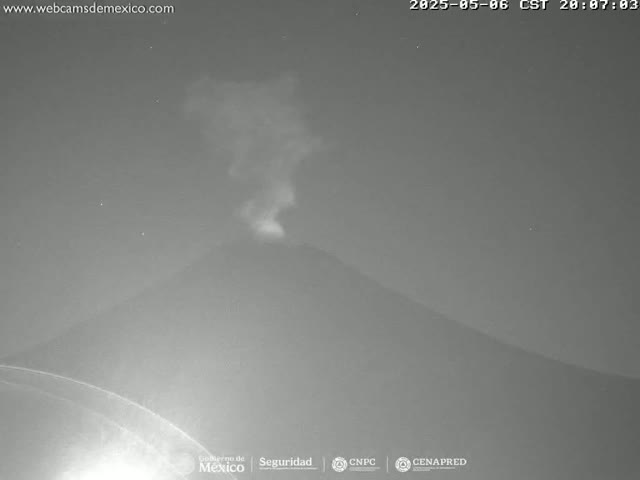 A nighttime, low-light image shows a plume of smoke or ash rising from a dark, volcano-shaped mountain.
