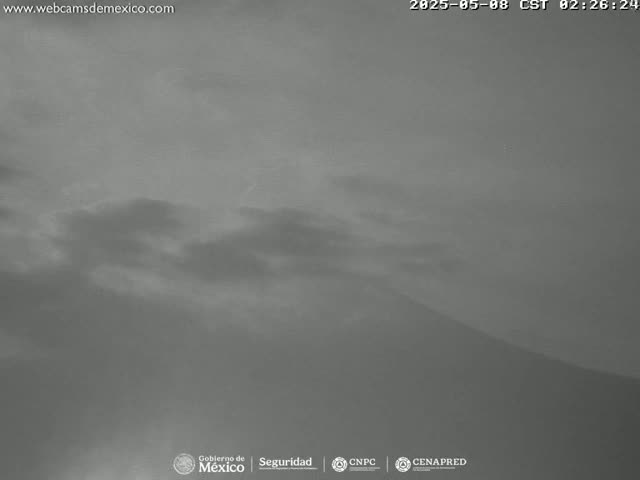 A grayscale image shows a mountain under a cloudy, overcast sky.