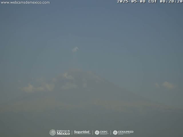 A hazy, mostly clear sky obscures a distant mountain under a few scattered clouds.