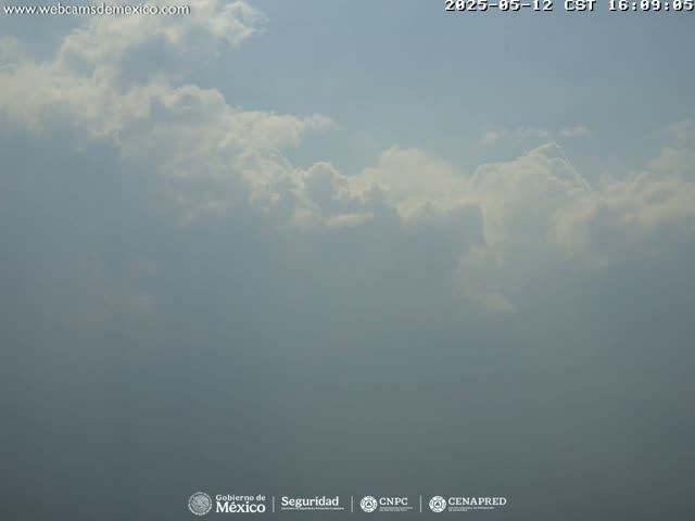 A hazy sky with scattered cumulus clouds is visible.