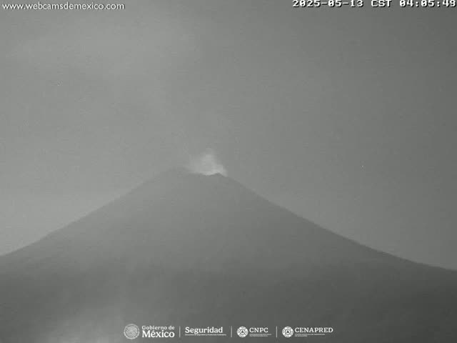 A grayscale image shows a volcano emitting a small plume of smoke under a hazy sky.