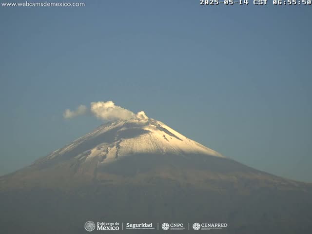 A snow-capped volcano emits a small plume of smoke under a clear blue sky.