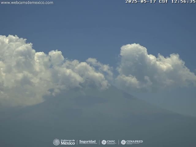 A partly cloudy sky with fluffy cumulus clouds obscures a hazy mountain range in the distance.