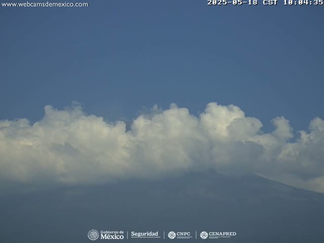A mountain is partially obscured by a large, low-lying mass of fluffy white clouds under a clear blue sky.