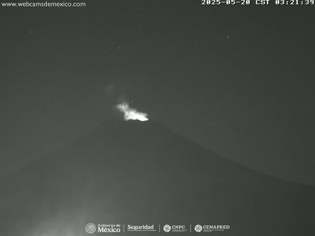 A nighttime, low-light image shows a volcano erupting with a small plume of light-colored ash rising into the dark sky.