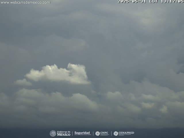 A mostly cloudy sky with a few brighter, puffy clouds is visible over a dark ocean or body of water.
