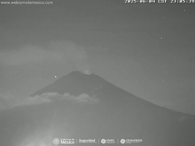 A nighttime, low-light image shows a volcano emitting a plume of smoke under a dark, clear sky.