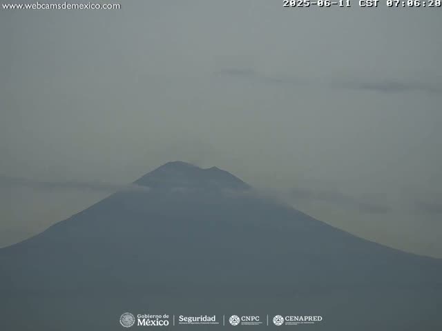A large, dark mountain is partially obscured by a light gray haze under a mostly clear sky.