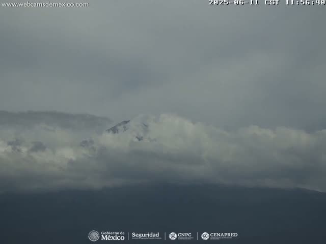 A mountain peak is partially obscured by a thick layer of clouds under an overcast sky.